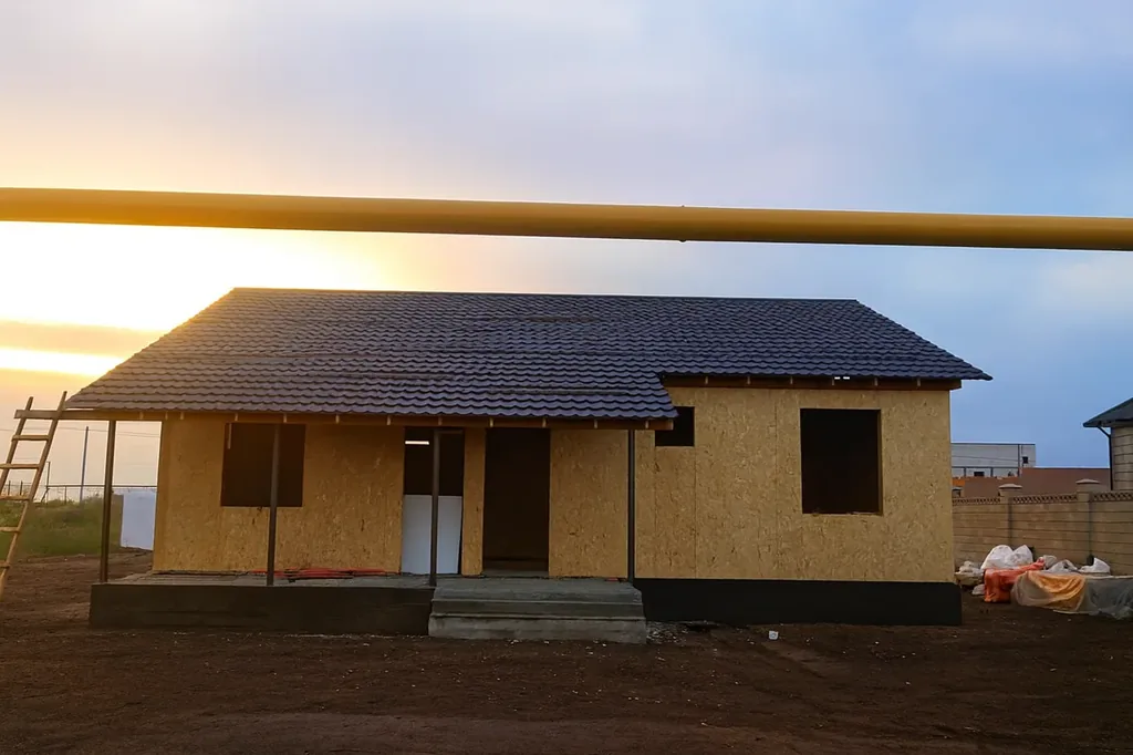 Дом «Данияр» 130 м², Астана, 2026: фасад под готовой кровлей, вынос крыши над террасой опирается на стойки, забетонированы ступени крыльца