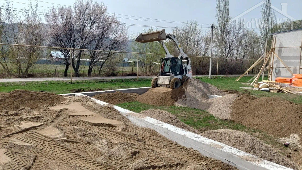 Мини-погрузчик Bobcat засыпает песчаную подушку внутрь ленточного фундамента