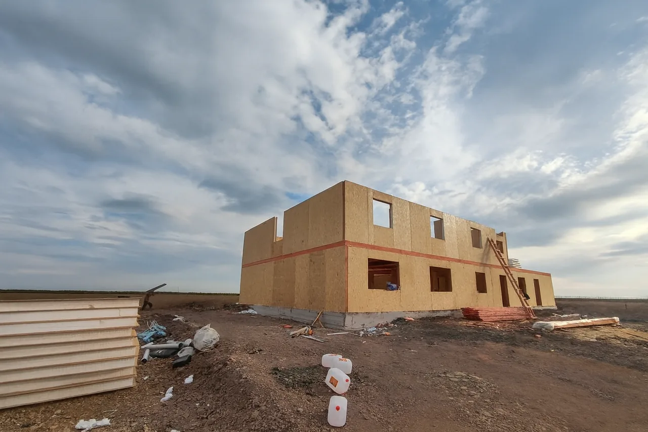 Общежитие «Доссан» 550 м², Астана, 2026: собраны стены первого и второго этажей из СИП-панелей, по периметру идёт пояс межэтажной обвязки, у стены — приставная лестница и пачка панелей