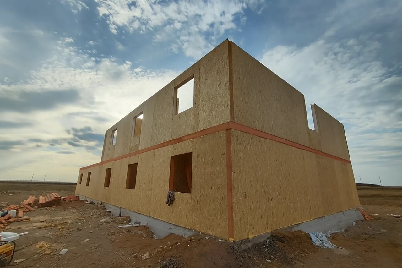 Общежитие «Доссан» 550 м², Астана, 2026: угол здания вблизи — стены двух этажей собраны, видны проёмы под окна и двери и красный пояс обвязки между этажами