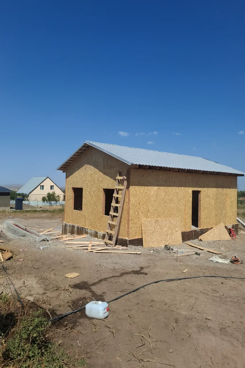 Дом «Пётр» 54 м², Каскелен, 2026: на собранной коробке из СИП-панелей смонтирована двускатная кровля из металлочерепицы с подшитыми свесами, оставлены проёмы под окна и входную дверь