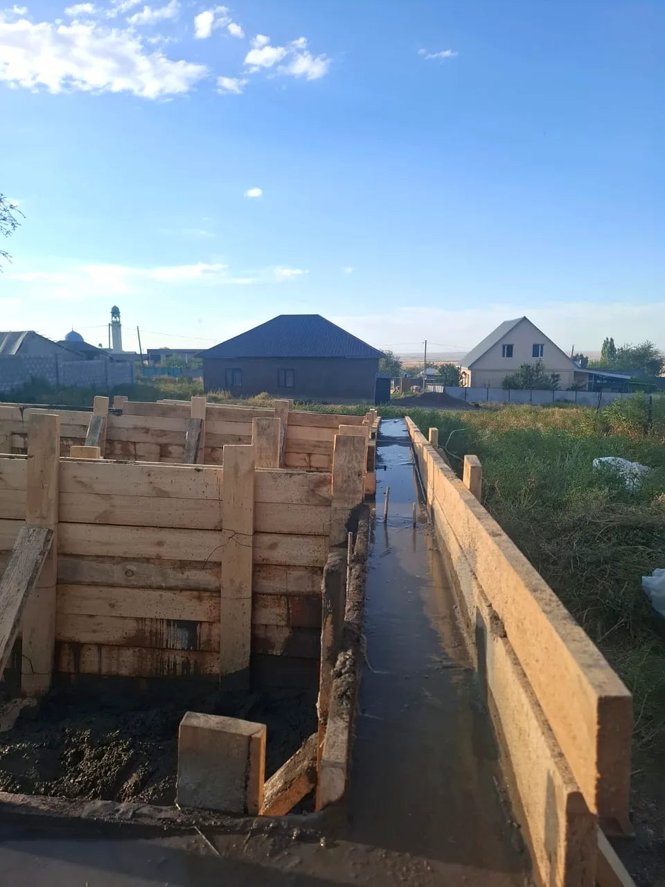 Дом «Пётр» 54 м², Каскелен, 2026: вид вдоль залитой ленты фундамента, щиты опалубки и распорки по всей длине
